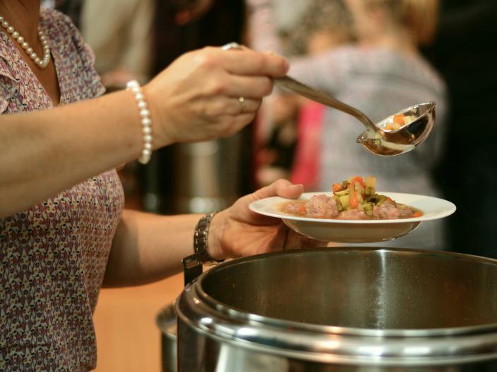 eine Frau füllt aus einem Topf einen Suppenteller mit Suppe