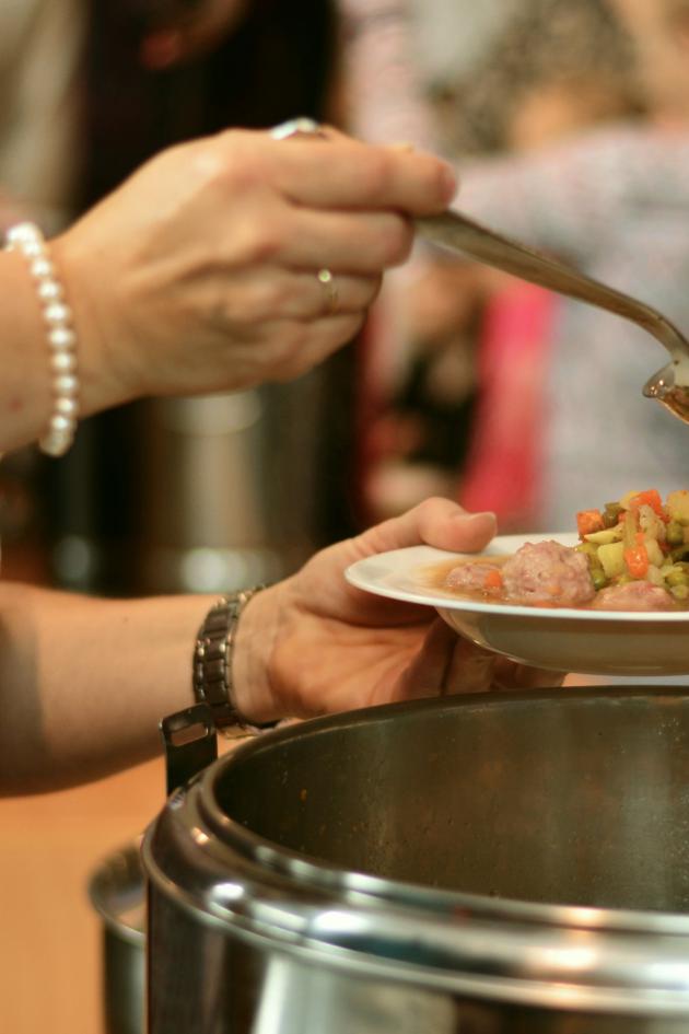 eine Frau füllt aus einem Topf einen Suppenteller mit Suppe