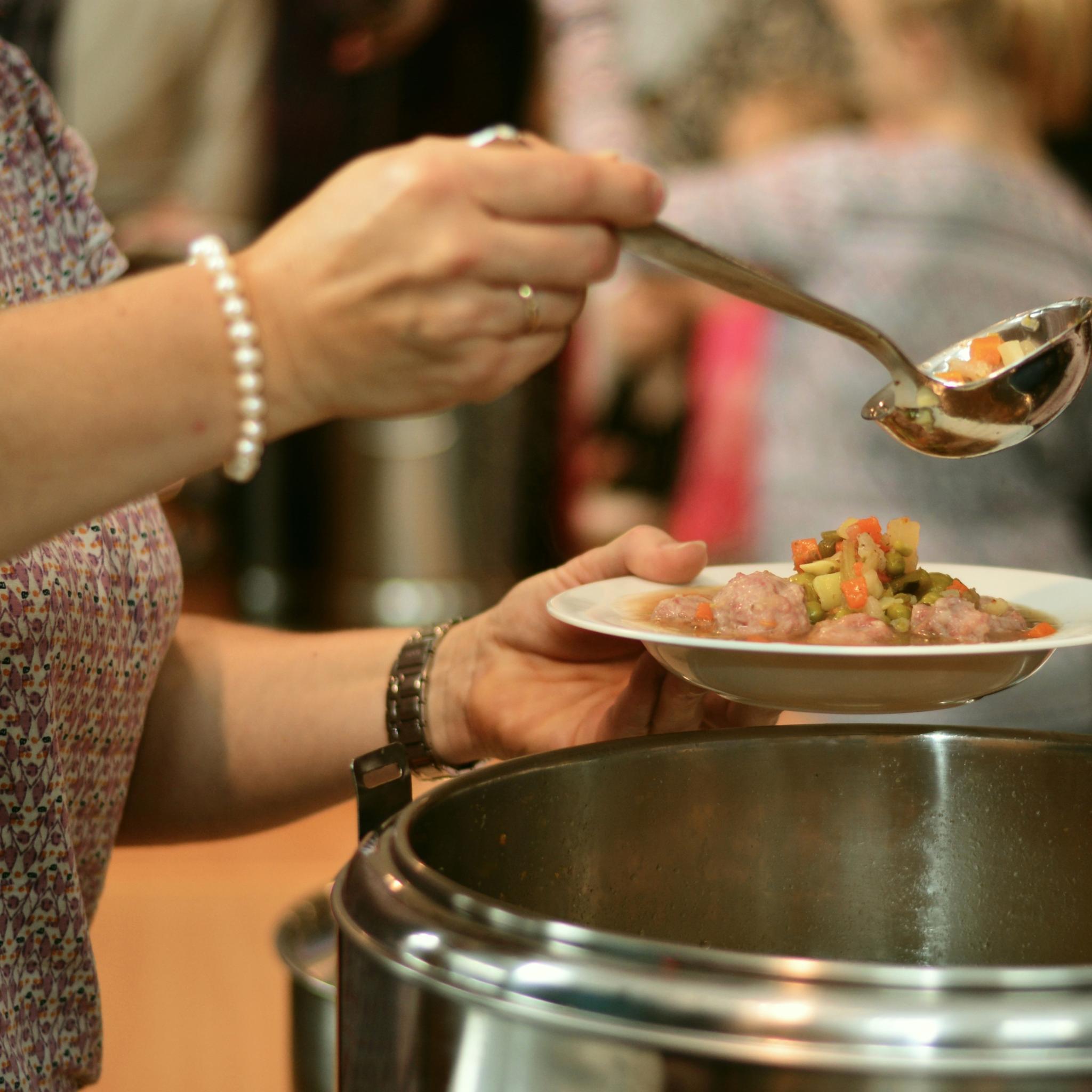 eine Frau füllt aus einem Topf einen Suppenteller mit Suppe