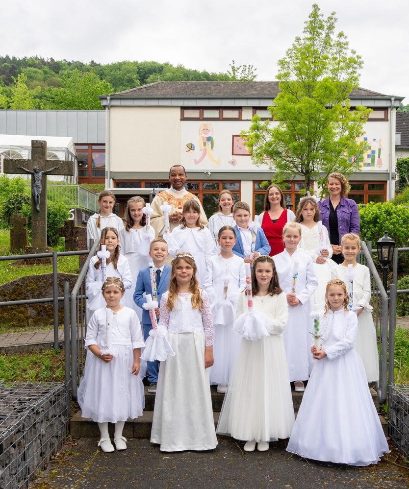 zu sehen sind 13 Kommunionkinder, 2 Jungen und 11 Mädchen, dahinter Pater Pater Chukwuma, die Messdienerinnen und Katechetinnen