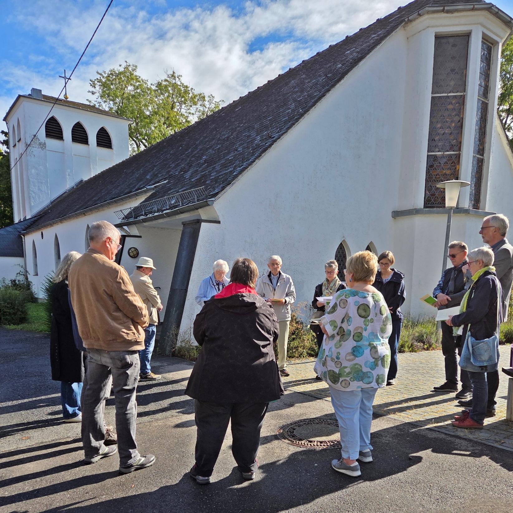 Pilgerspaziergang Beginn ab der Kirche St. Beatus mehrere Frauen und Männer stehen im Kreis zu einer Andacht, im Hintergrund eine Kirche