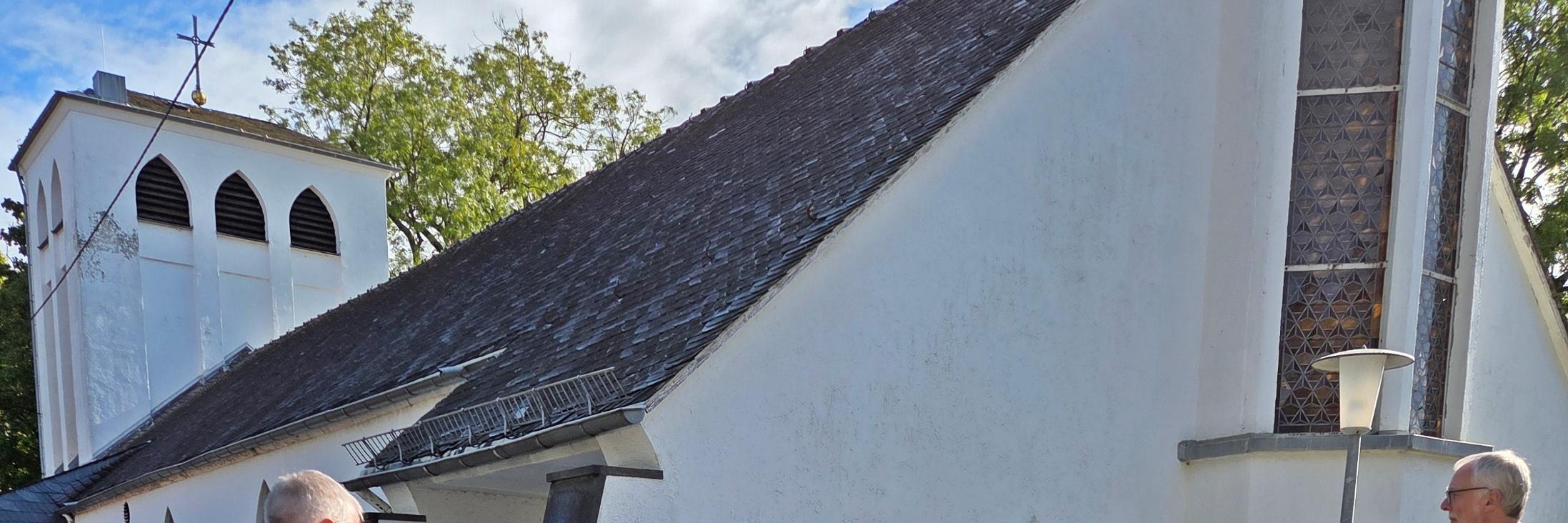 mehrere Frauen und Männer stehen im Kreis zu einer Andacht, im Hintergrund eine Kirche