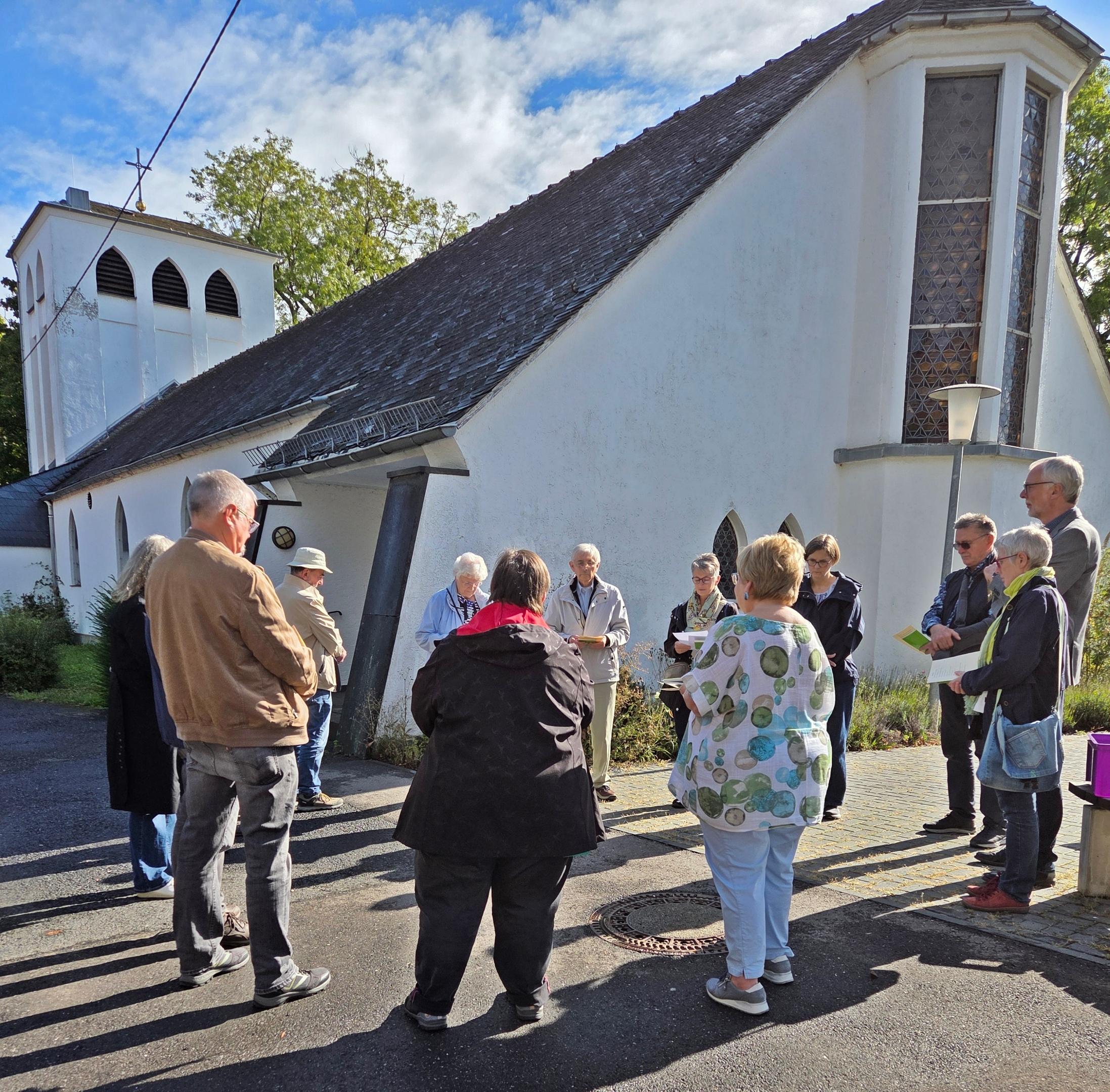 mehrere Frauen und Männer stehen im Kreis zu einer Andacht, im Hintergrund eine Kirche