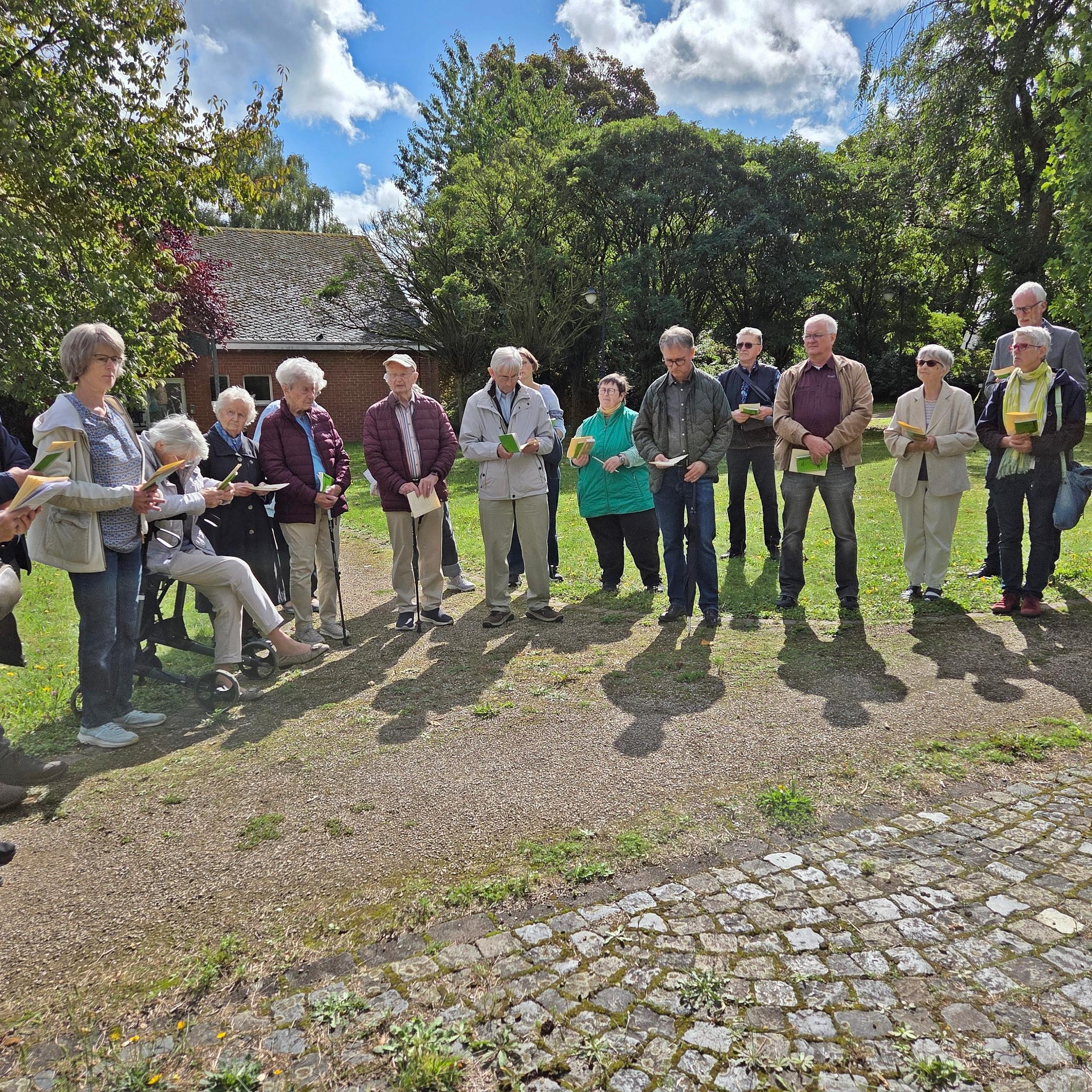 Statio im Park eine Gruppe von Menschen steht in einem Halbkreis mit Textblättern in der Hand, in einem Park