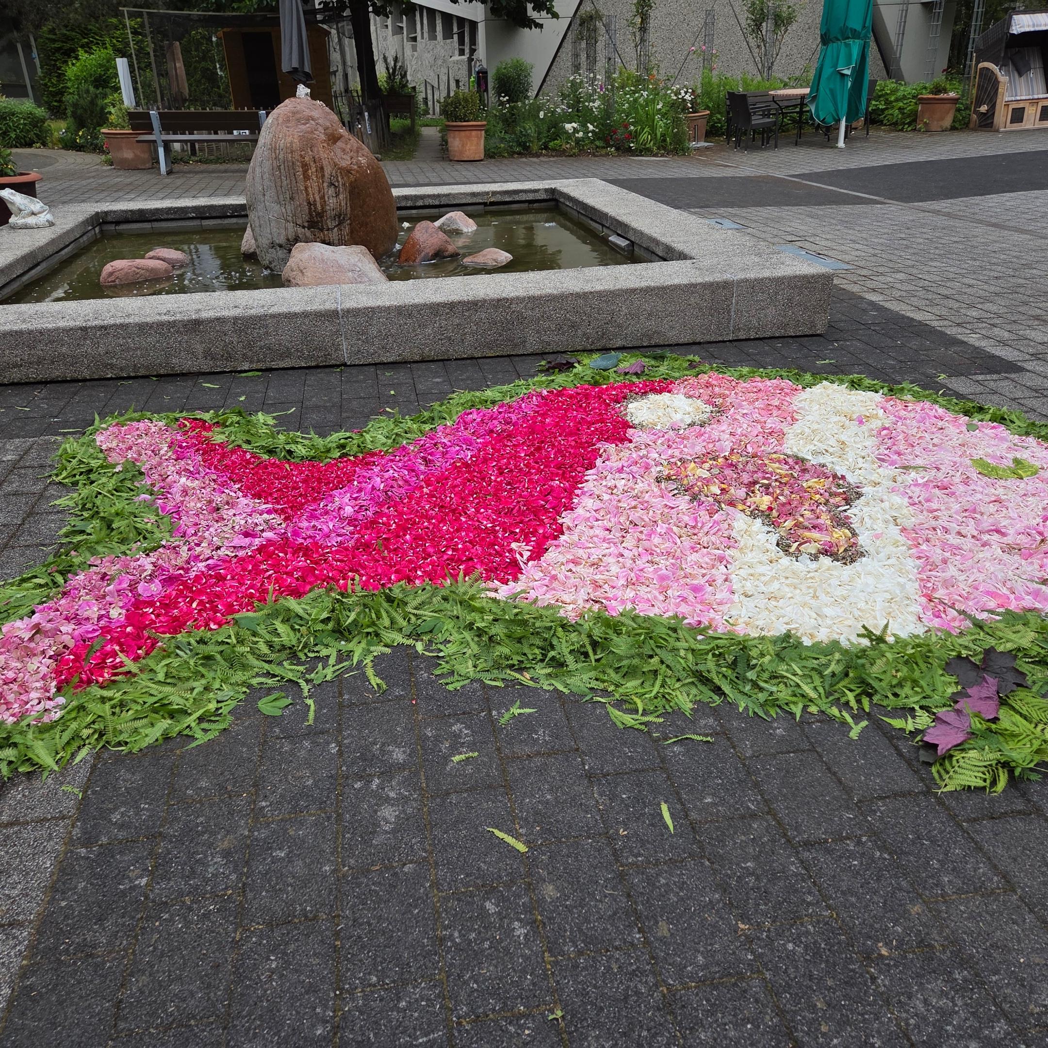 Ein Fisch als Blumenteppich. Kontur grün, Kopf und Körper in den Farben rosa und weiß übergehend zum Schwanz pink und rosa