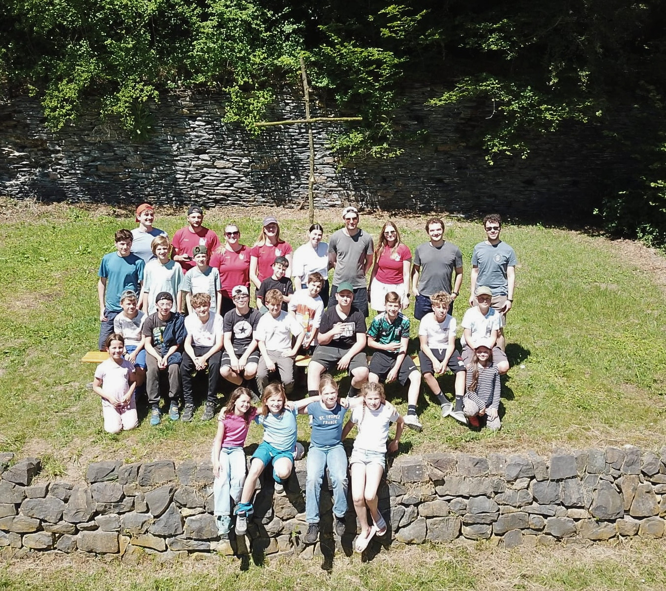 28 Kinder, Jugendliche und Betreuer auf einem Wiesenhang als Gruppe vor einem Kreuz fotografiert