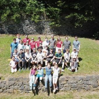 28 Kinder, Jugendliche und Betreuer auf einem Wiesenhang als Gruppe vor einem Kreuz fotografiert
