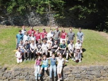 28 Kinder, Jugendliche und Betreuer auf einem Wiesenhang als Gruppe vor einem Kreuz fotografiert