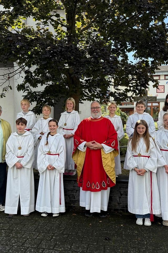 Pfarrer Michael Frevel in rotem lithurgischen Gewand der Mitte von einer Gruppe junger Ministranten