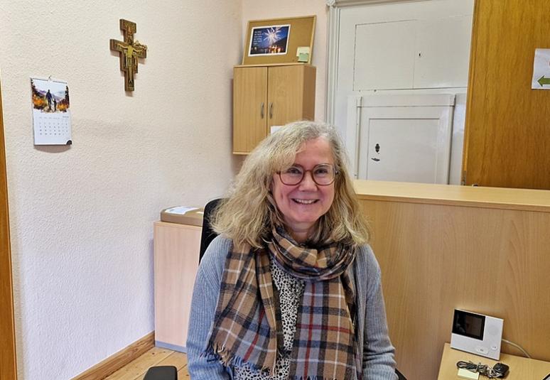 Pfarrsekretärin Barbara Stutzer im Büro, im Hintergrund ein Kreuz