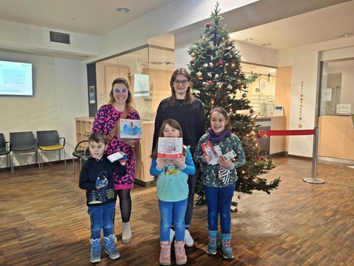 Drei Kinder und zwei Frauen stehen im Foyer einer Klinik vor einem Weihnachtsbaum, in den Händen halten sie die Spenden