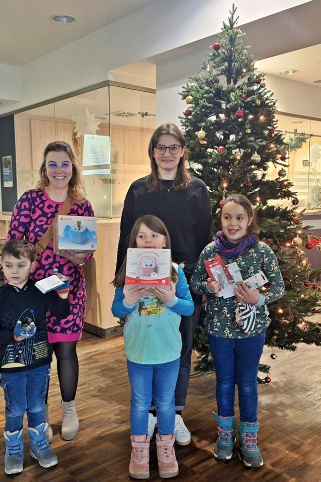 Drei Kinder und zwei Frauen stehen im Foyer einer Klinik vor einem Weihnachtsbaum, in den Händen halten sie die Spenden