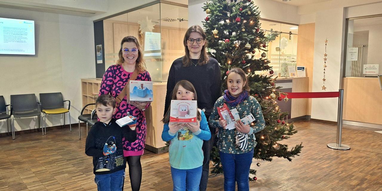 Drei Kinder und zwei Frauen stehen im Foyer einer Klinik vor einem Weihnachtsbaum, in den Händen halten sie die Spenden