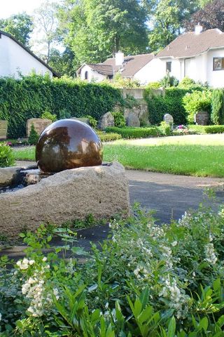 Blick auf einen Brunnen mit Sitzbank, im Hintergrund sind Grabstätten vor der Friedhofsmauer zu sehen