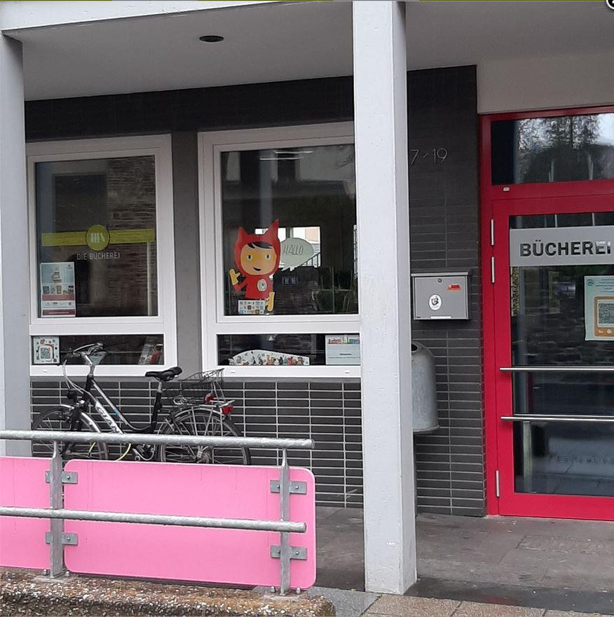 Blick auf die Eingangstür und 2 Fenster, davor steht ein Fahrrad. Ein Fenster ist mit dem Schriftzug der Bücherei beklebt