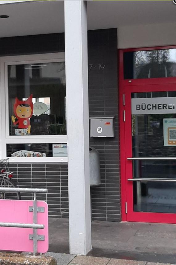 Blick auf die Eingangstür und 2 Fenster, davor steht ein Fahrrad. Ein Fenster ist mit dem Schriftzug der Bücherei beklebt
