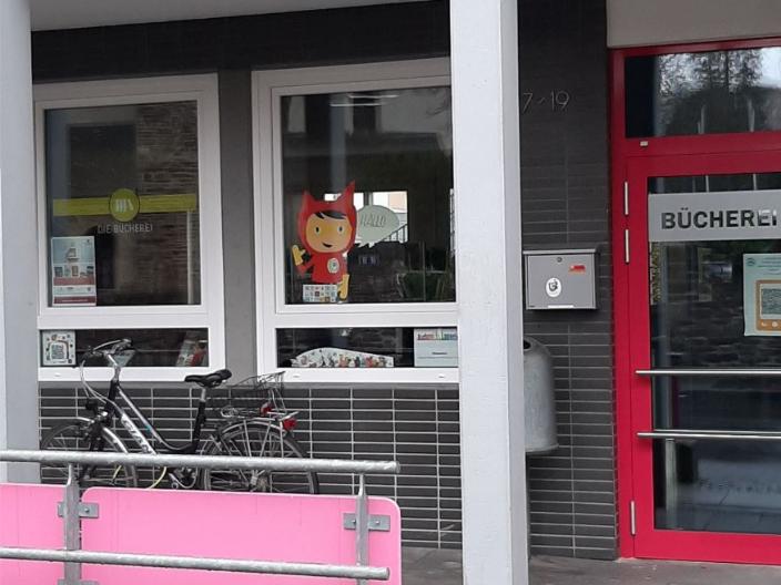 Blick auf die Eingangstür und 2 Fenster, davor steht ein Fahrrad. Ein Fenster ist mit dem Schriftzug der Bücherei beklebt