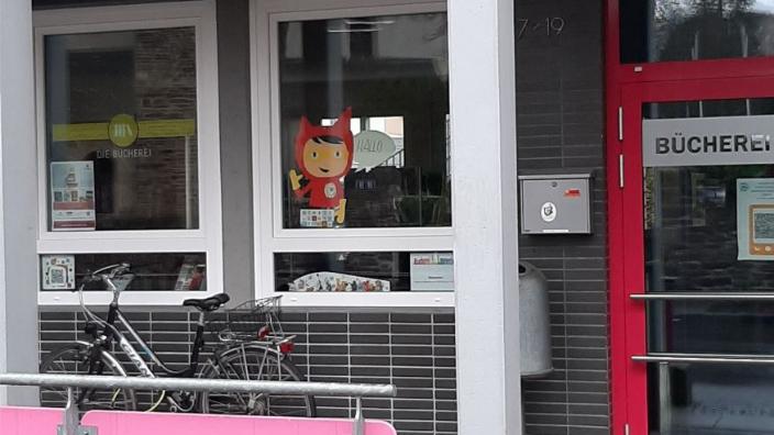 Blick auf die Eingangstür und 2 Fenster, davor steht ein Fahrrad. Ein Fenster ist mit dem Schriftzug der Bücherei beklebt