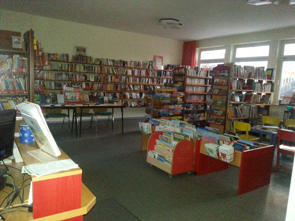 Blick auf den Innenraum der Bücherei mit Regalen links die Theke
