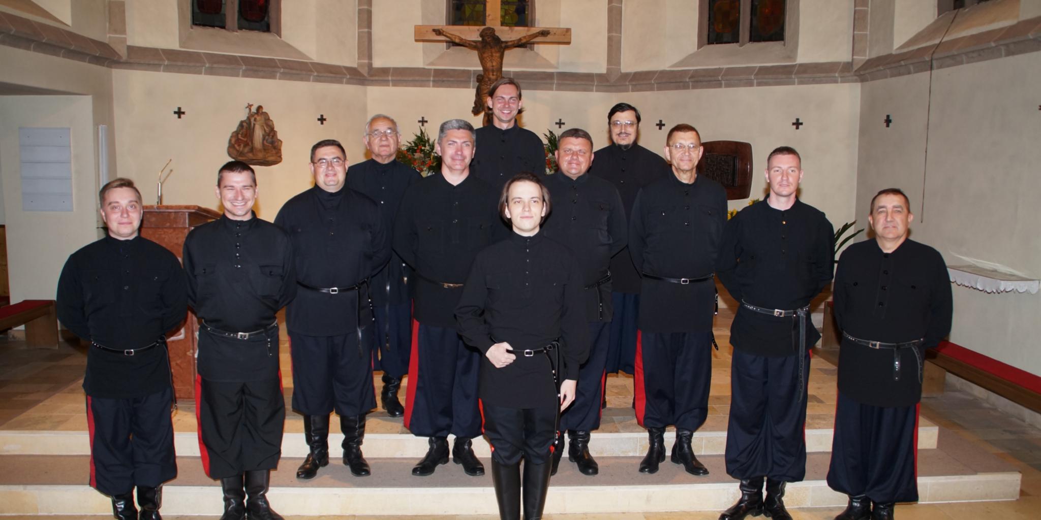 Don Kosaken Chor Zwölf Männer ganz in schwarz gekleidet stehen im Chorraum einer Kirche vor einem Kreuz