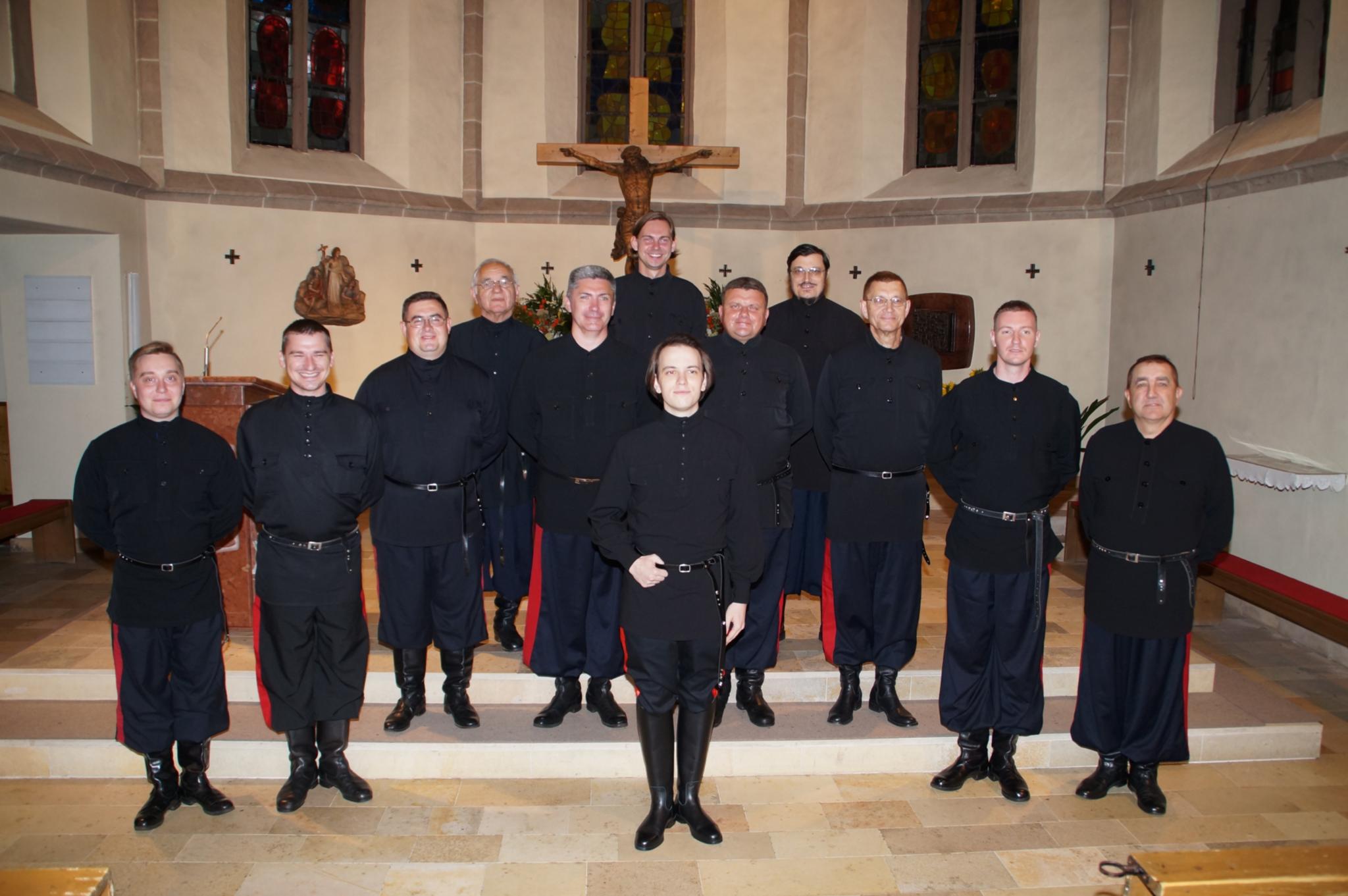 Don Kosaken Chor Zwölf Männer ganz in schwarz gekleidet stehen im Chorraum einer Kirche vor einem Kreuz