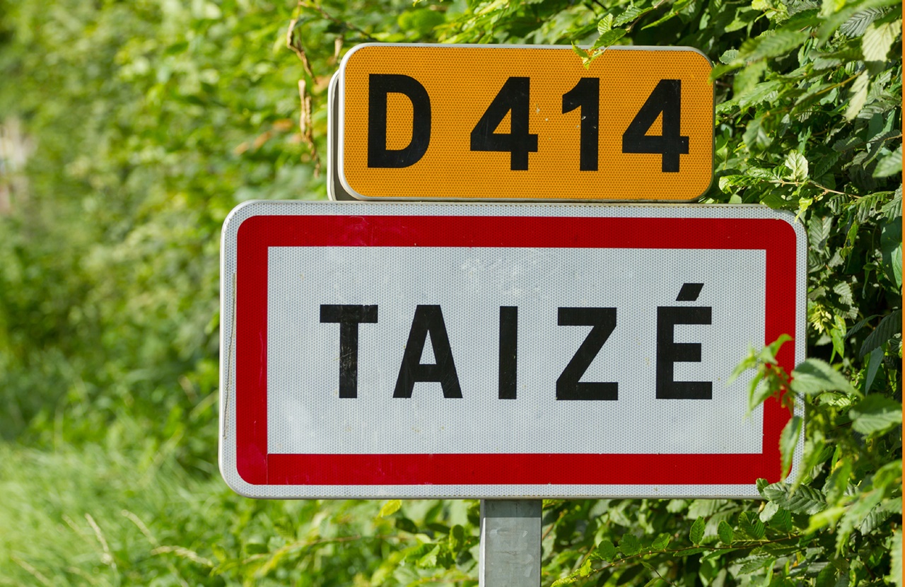 Straße D414 mit Ortsschild von Taize im Hintergrund Blätter und Wiese