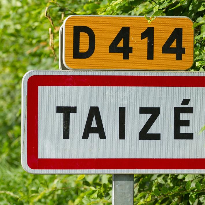 Straße D414 mit Ortsschild von Taize im Hintergrund Blätter und Wiese