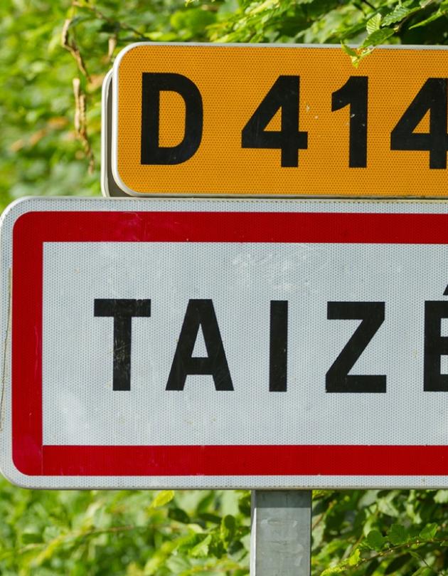 Straße D414 mit Ortsschild von Taize im Hintergrund Blätter und Wiese
