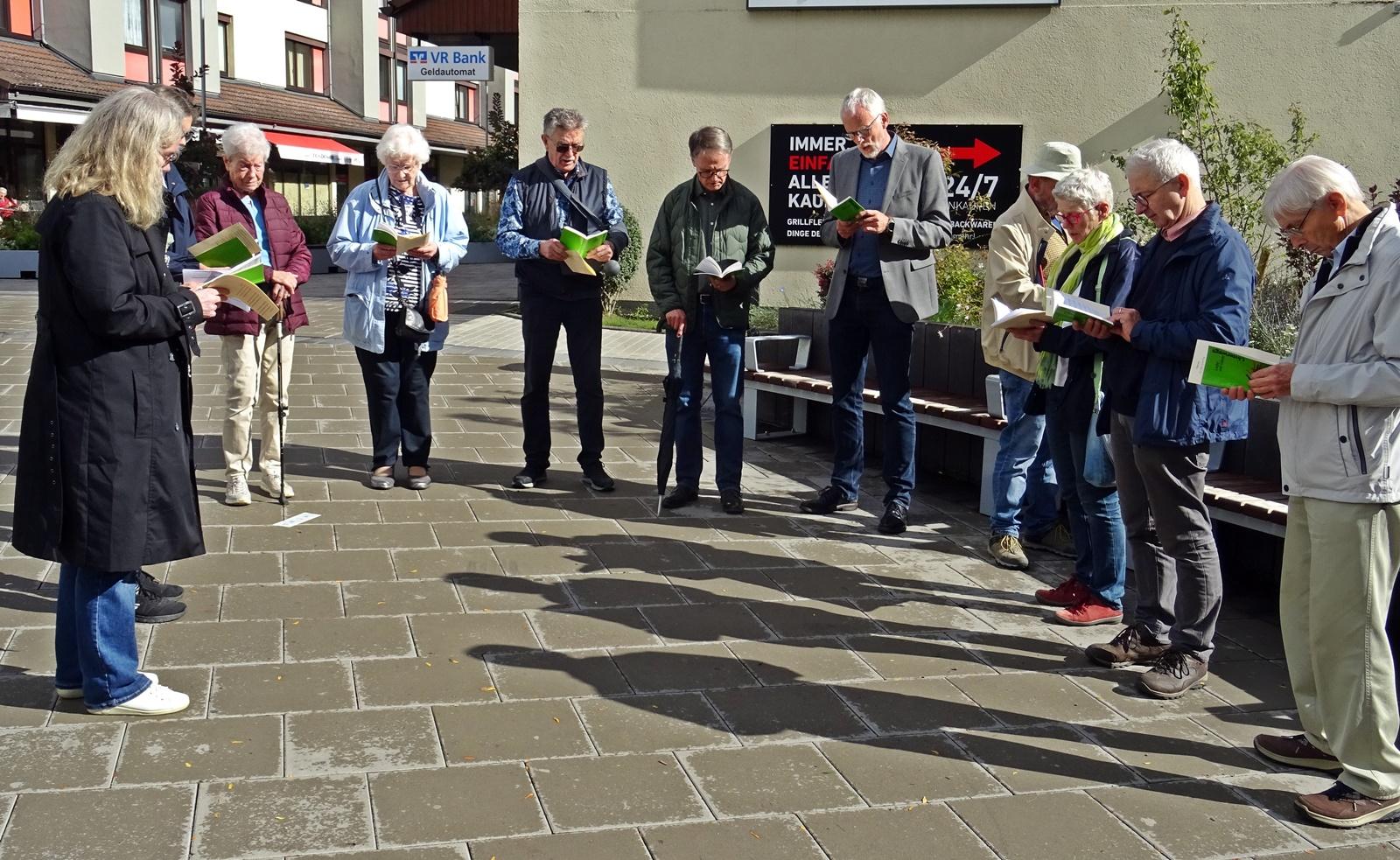 mehrere Frauen und Männer stehen im Halbkreis und schauen auf Blätter in ihrer Hand