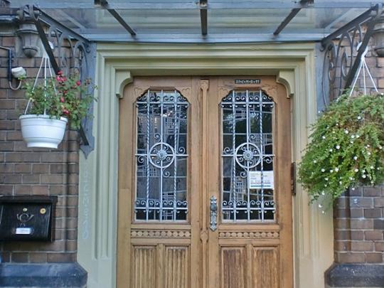 Man sieht die Tür des Pfarrhauses sowie drumherum Backsteine des Gebäudes sowie besondere Fenster über der Tür