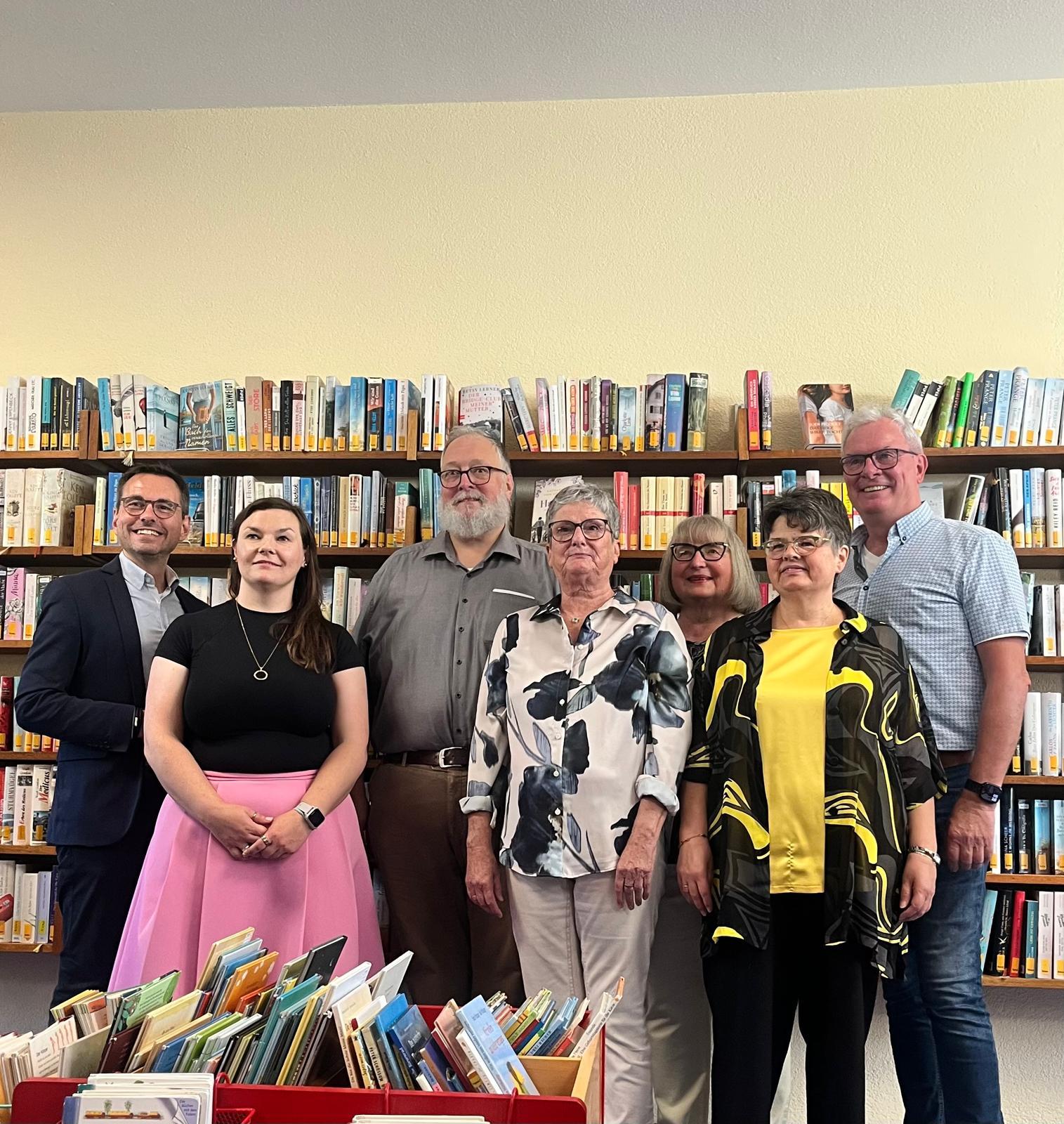 Feierlich gekleidete Personen vor Bücherregalen, davor Kisten mit Büchern