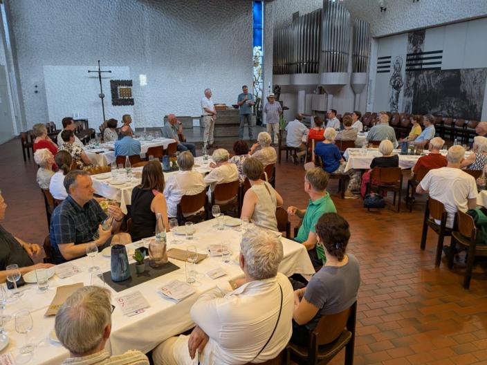 An sechs großen mit Wein-, Wassergläsern und Tellern eingedeckten Tischen sitzen Teilnehmer der Veranstaltung Wein und Brot und lauschen den Referenten