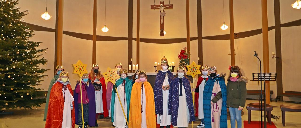 Eine Gruppe Kinder als Sternsinger verkleidet in einer Kirche unter einem Kreuz