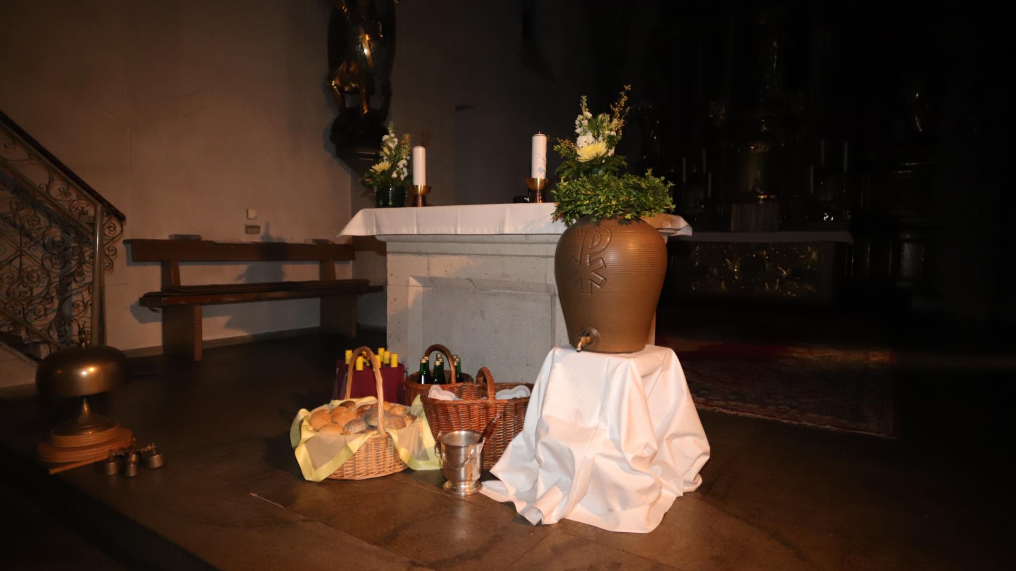 Vor dem Altar der St. Laurentiuskirche in Koblenz stehen Körbe gefüllt mit Osterbrötchen, Traubensaft- und Weinflaschen, Weihwasserkessel und Weihwasserbehälter