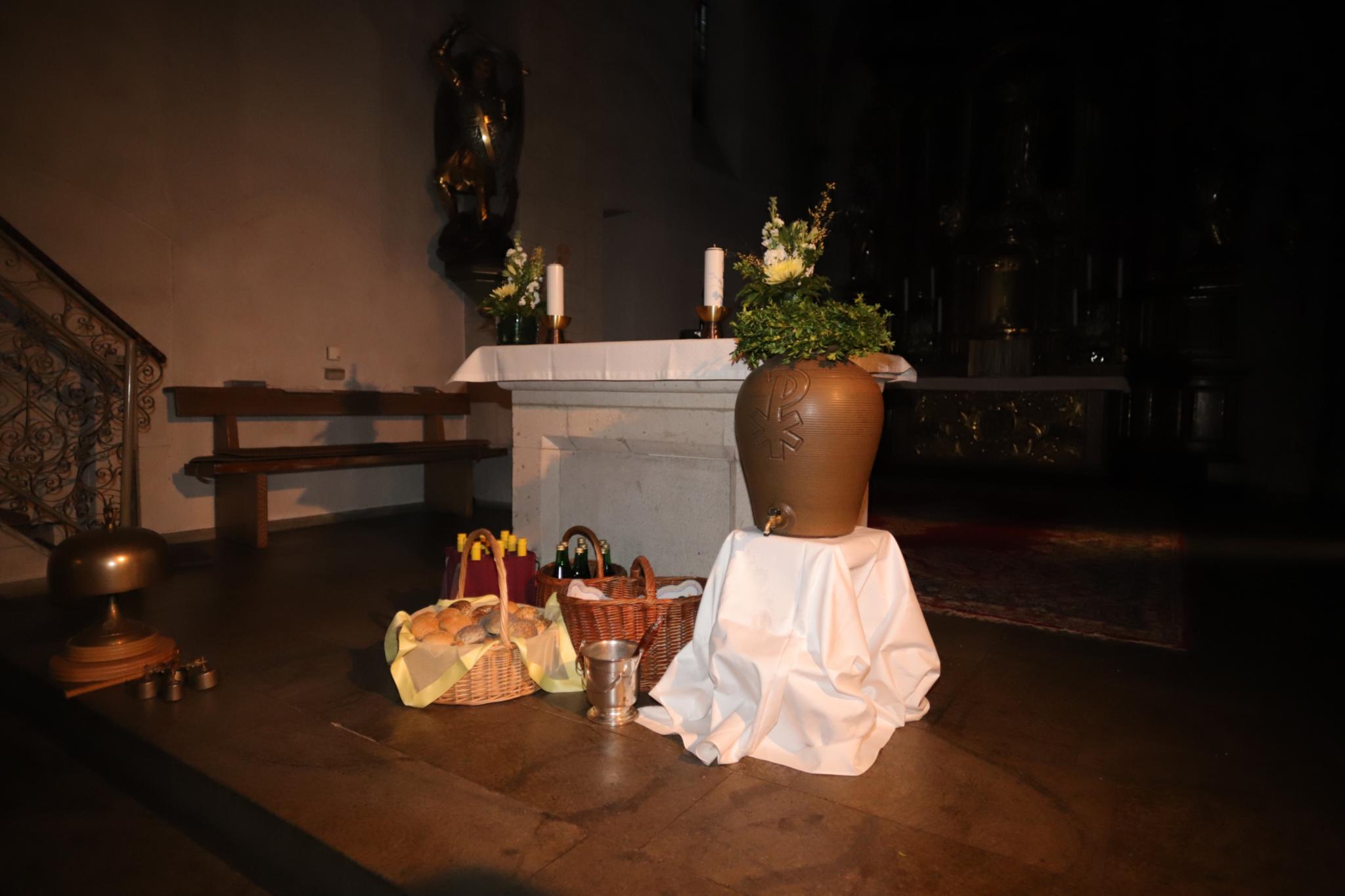 Vor dem Altar der St. Laurentiuskirche in Koblenz stehen Körbe gefüllt mit Osterbrötchen, Traubensaft- und Weinflaschen, Weihwasserkessel und Weihwasserbehälter