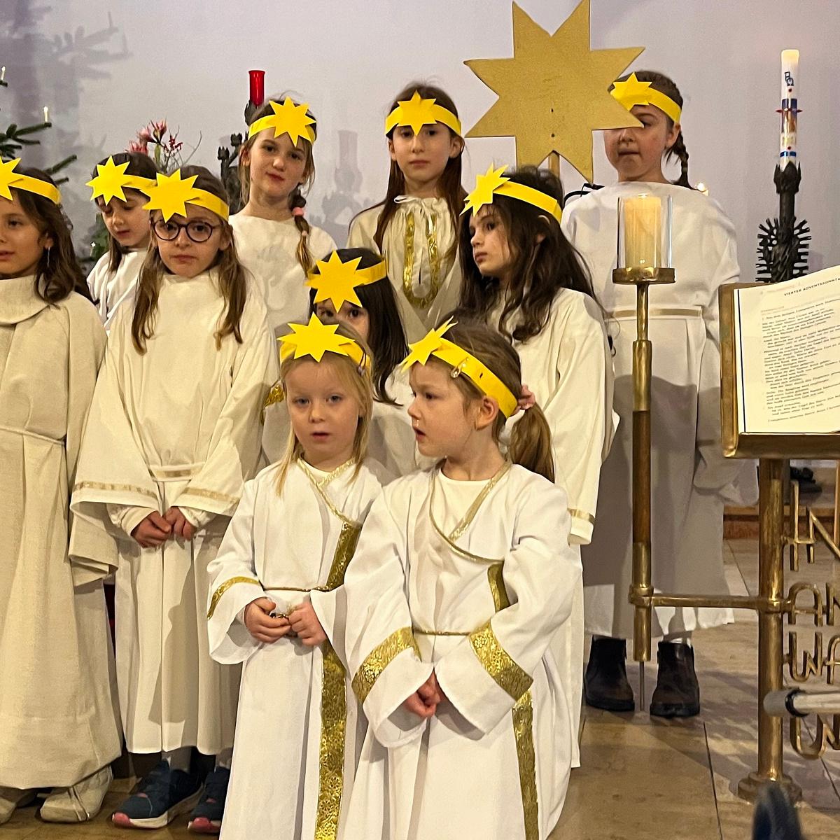 Neun Kinder verschiedenen Alters als Engel gekleidet, mit einem Stirnband mit einem Stern, im Altarraum einer Kirche