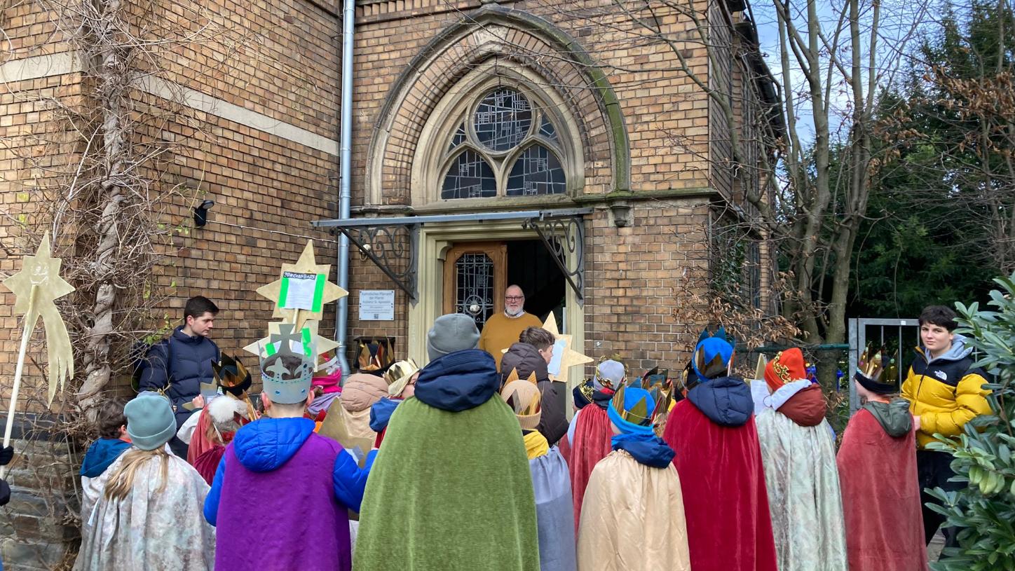 Eine Gruppe Kinder als Sternsinger gekleidet von hinten, in der Tür eines historischen Hauses steht ein Mann
