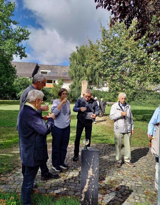 mehrere Personen stehen im Halbkreis in einem Park, ein Glas Wein in der Hand