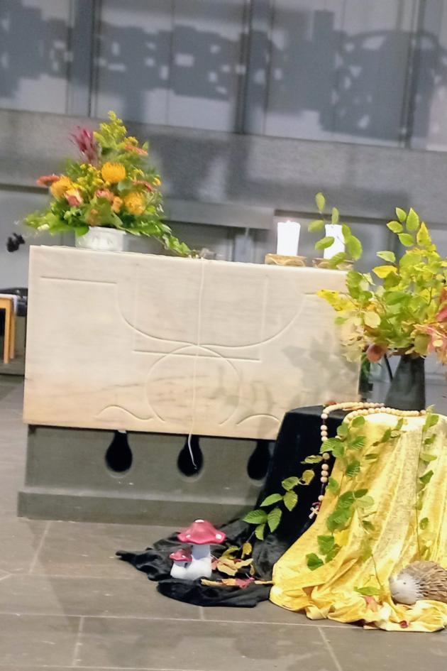 Altar in der St. Franziskuskirche mit Sonnenblumen geschmückt davor ein Tisch, bedeckt mit einem schwarzen und gelben Tuch, darauf eine Vase mit herbstlichen Zweigen. Um die Vase ein großer Rosenkranz gelegt
