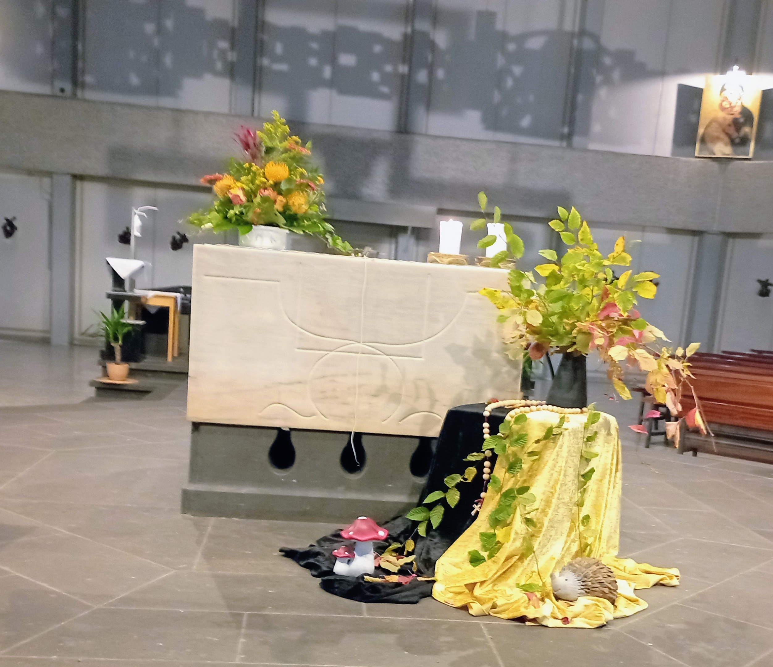 Altar in der St. Franziskuskirche mit Sonnenblumen geschmückt davor ein Tisch, bedeckt mit einem schwarzen und gelben Tuch, darauf eine Vase mit herbstlichen Zweigen. Um die Vase ein großer Rosenkranz gelegt