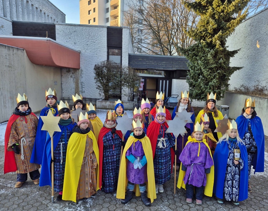 Eine Gruppe Kinder als Sternsinger gekleidet vor der St. Hedwig Kirche, Karthause. Im Hintergrund blauer Himmel