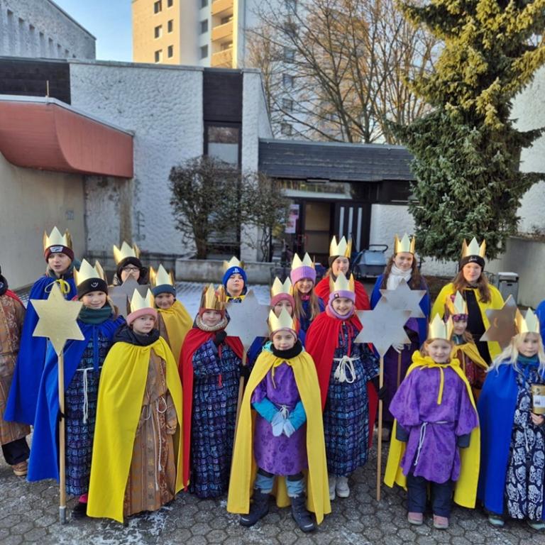 Eine Gruppe Kinder als Sternsinger gekleidet vor der St. Hedwig Kirche, Karthause. Im Hintergrund blauer Himmel