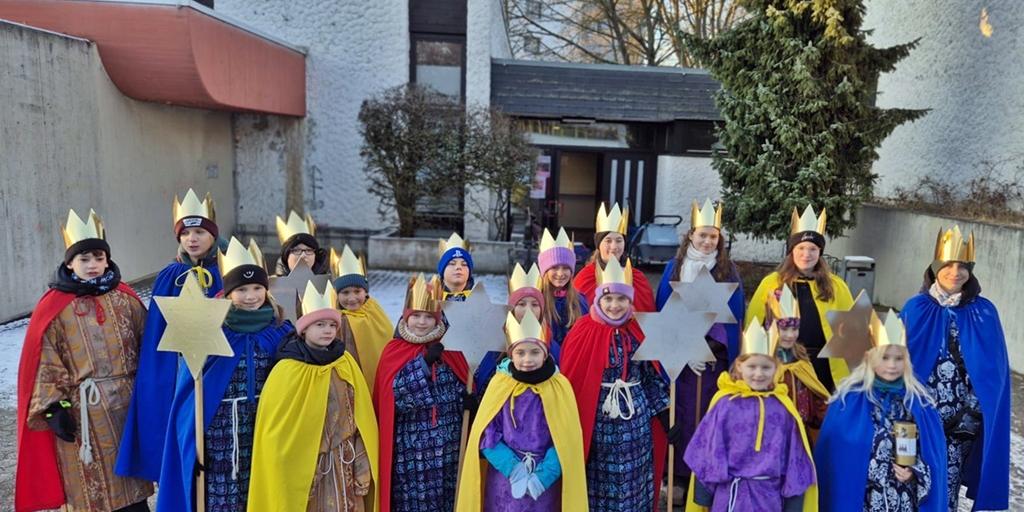 Eine Gruppe Kinder als Sternsinger gekleidet vor der St. Hedwig Kirche, Karthause. Im Hintergrund blauer Himmel