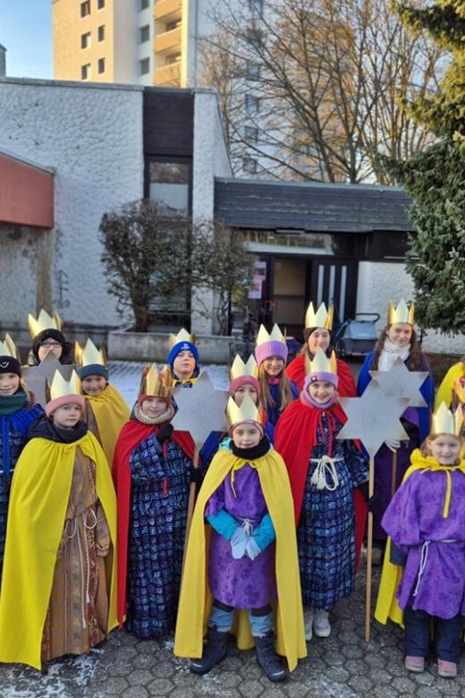 Eine Gruppe Kinder als Sternsinger gekleidet vor der St. Hedwig Kirche, Karthause. Im Hintergrund blauer Himmel