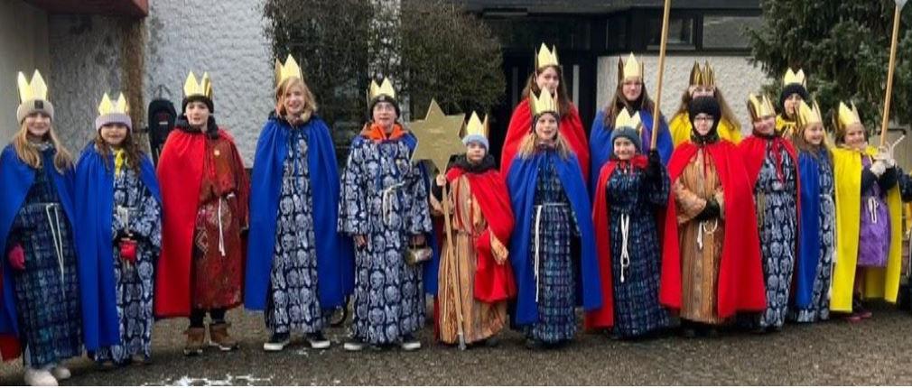 Eine Gruppe Kinder als Sternsinger gekleidetim Hintergrund die Kirche St. Hedwig