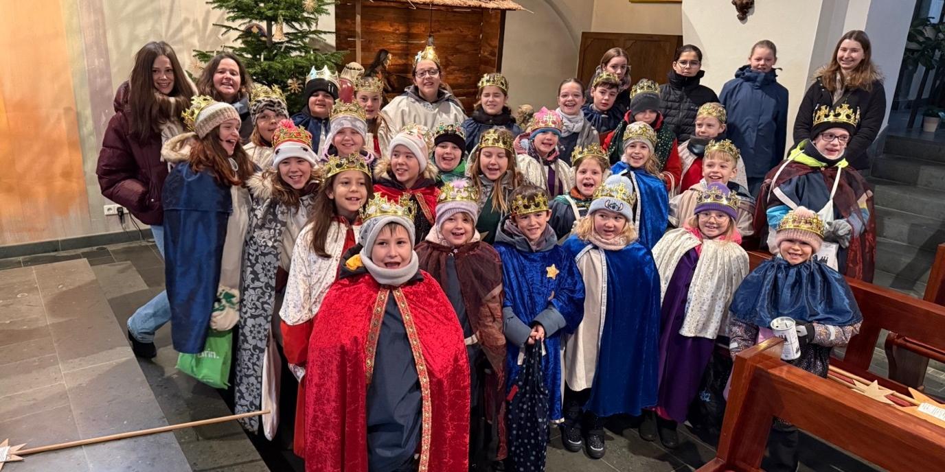 Eine fröhliche Sternsingergruppe mit ihren Betreuern,  vor der Krippe der St. Martinus Kirche in Lay