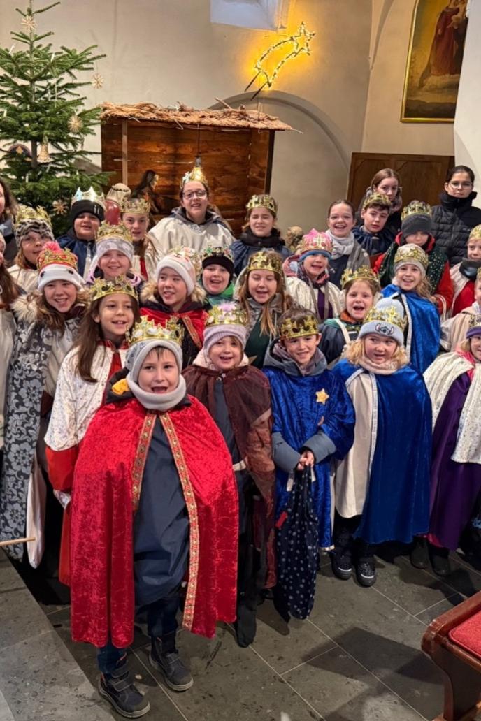 Eine fröhliche Sternsingergruppe mit ihren Betreuern,  vor der Krippe der St. Martinus Kirche in Lay