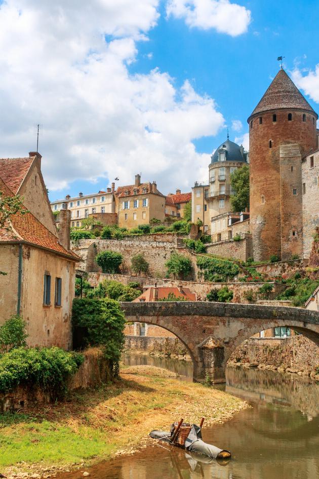 Zu sehen ist eine Ansicht der Stadt Semur, die  beidseitig an einem Fluss liegt über den eine mittelalterliche Brücke führt. Idylisch, malerisch sind mittelalterliche Gebäude und prominent ein Turm zu sehen.