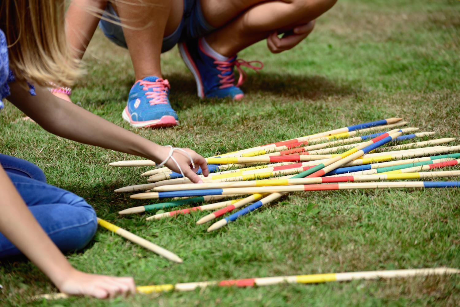 auf einem Rasen liegen Gartenmikadostangen, von zwei spielenden Kindern sind Hände und Füße zu sehen