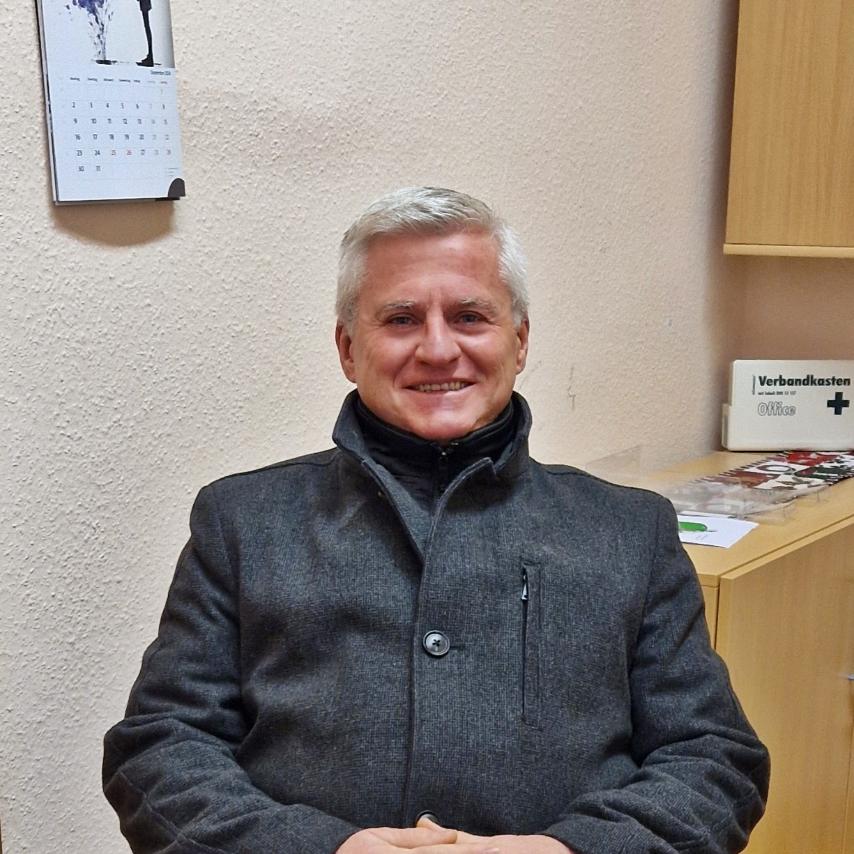 Jörg Stein sitzend im Bürostuhl, über ihm ein Kreuz an der Wand
